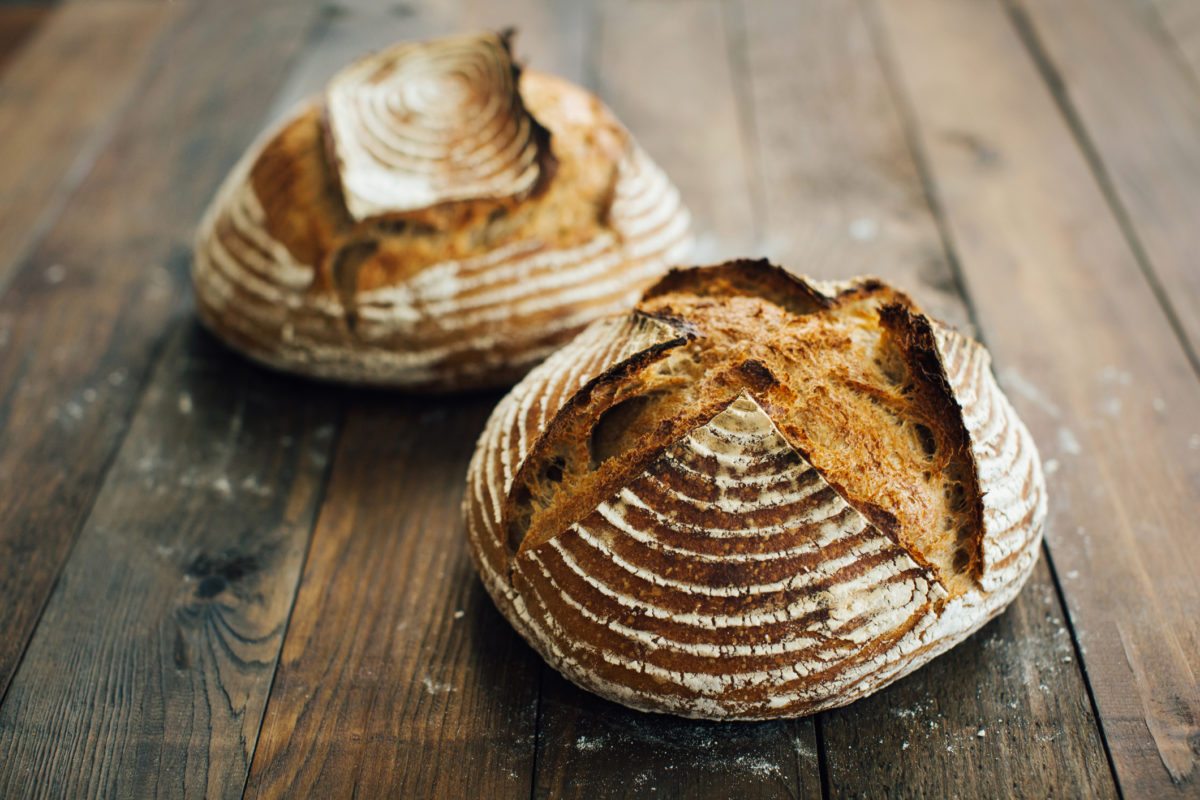 Two round loaves of artisanal bread with textured crusts sit on a wooden surface.