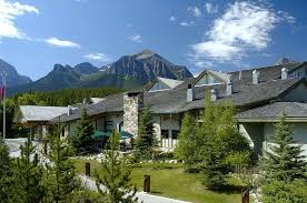 A building with a stone chimney surrounded by trees, set against a backdrop of mountains and a clear blue sky.