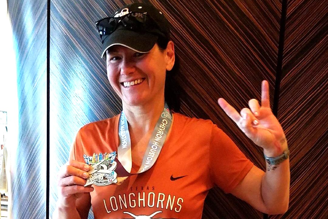 Person in an orange shirt holding a medal and making a hand gesture, smiling.