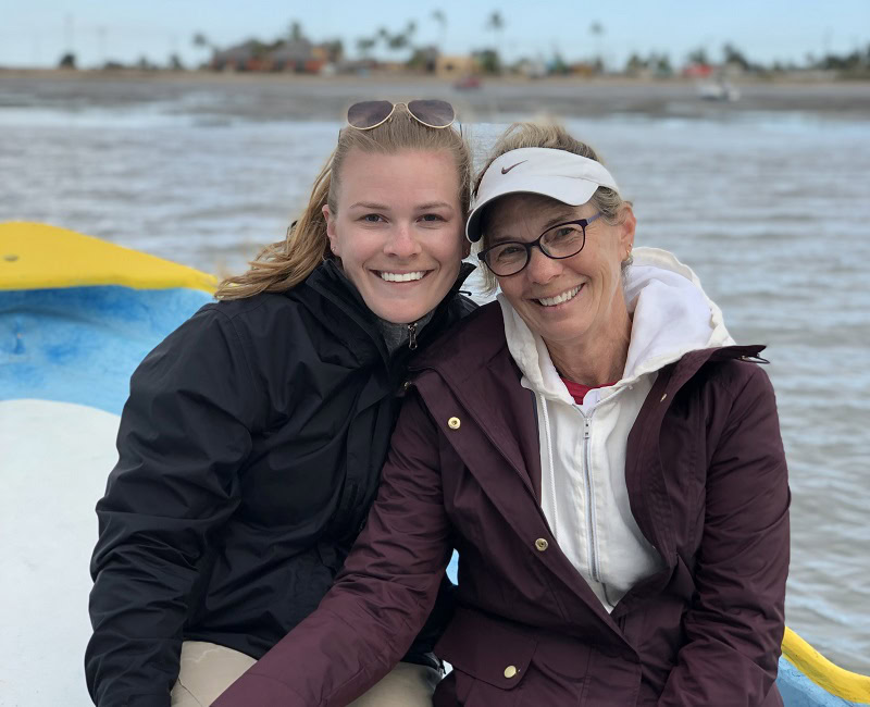 Two people smiling on a boat with a river and distant shoreline in the background.