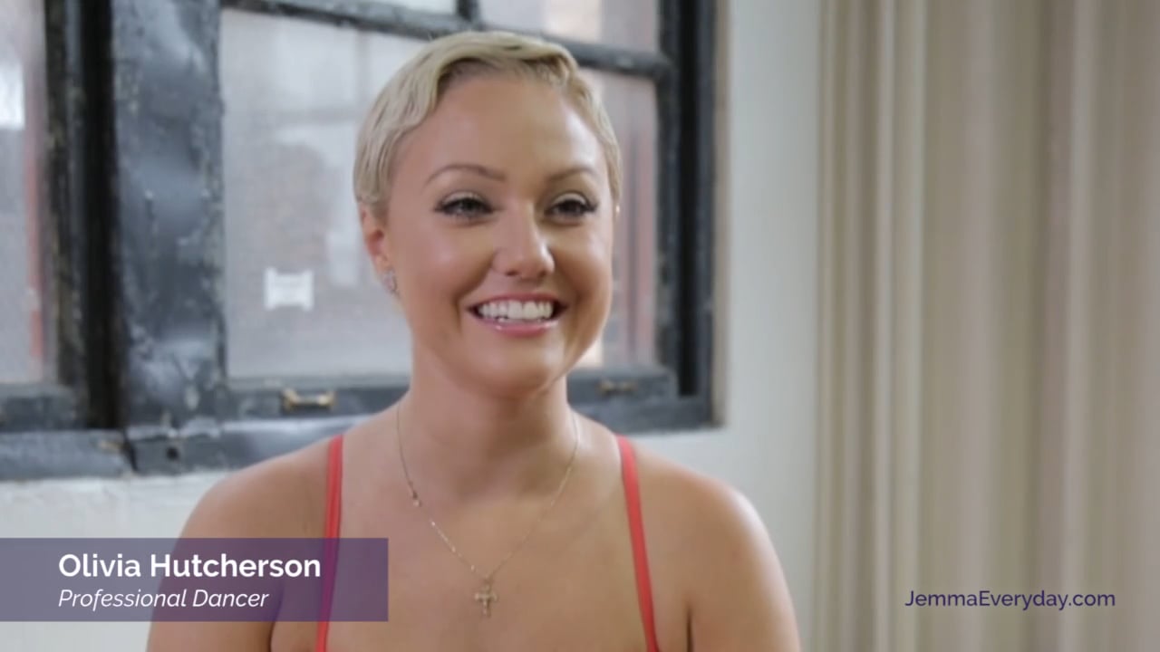 Smiling woman with short hair in a red top sits indoors, with text overlay showing her name and profession as a dancer.