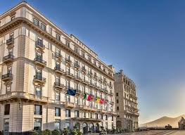 Historic multi-story hotel building with several flags on display, set against a clear blue sky, with a mountain visible in the background.