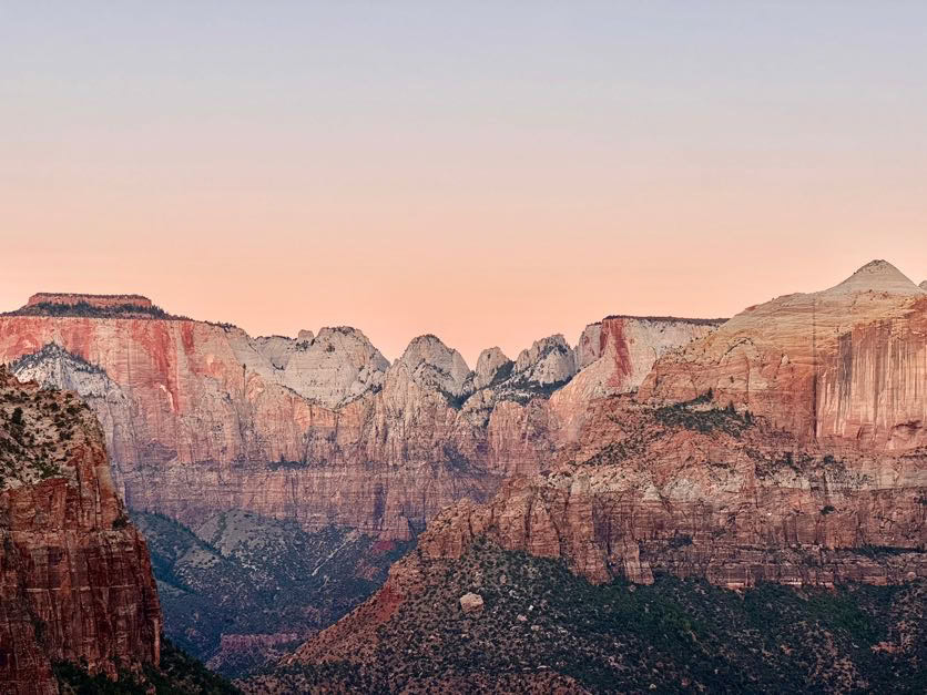 Rocky mountain range under a clear sky transitioning from pink to blue at sunset.