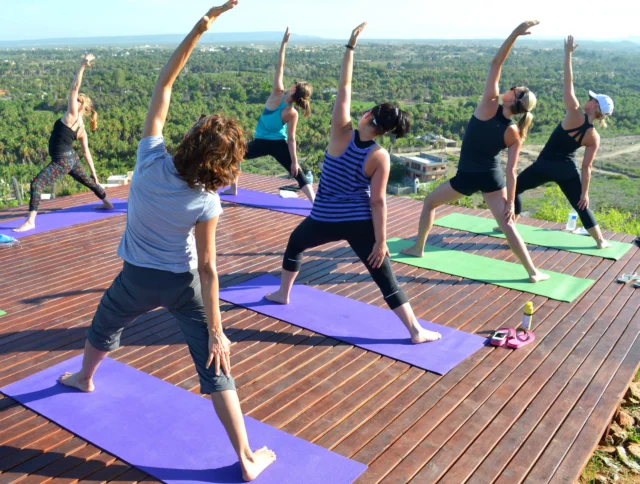 Group of people practicing yoga on a wooden deck outdoors, with a scenic view in the background.