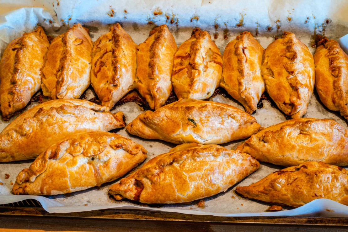 A tray of baked golden-brown pasties lined up on parchment paper.