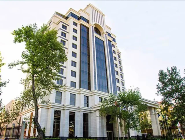 A tall, modern office building with large windows and trees in the foreground.