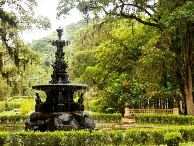 An ornate black fountain in a lush green garden surrounded by trees and shrubbery.