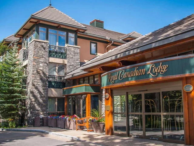 Exterior view of the Royal Canadian Lodge, featuring stone and wood architecture, with lush greenery and colorful flower planters.