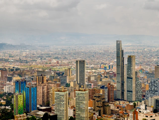 Aerial view of a bustling cityscape featuring modern skyscrapers and colorful buildings under a cloudy sky.