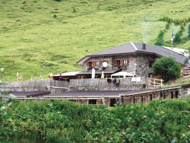 Stone building in a grassy hillside setting with wooden fences, flags, and outdoor seating area.