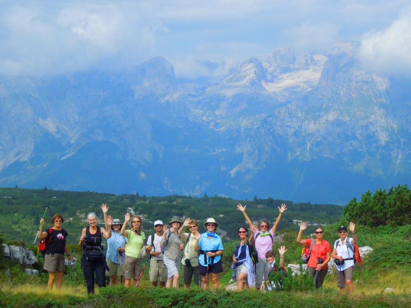A group of people posing with hiking gear in a lush green landscape, with mountains and a cloudy sky in the background.
