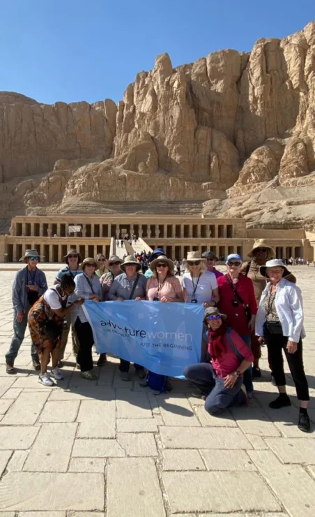 A group of people holding a "Future Women" banner stand in front of an ancient stone structure under a clear blue sky.