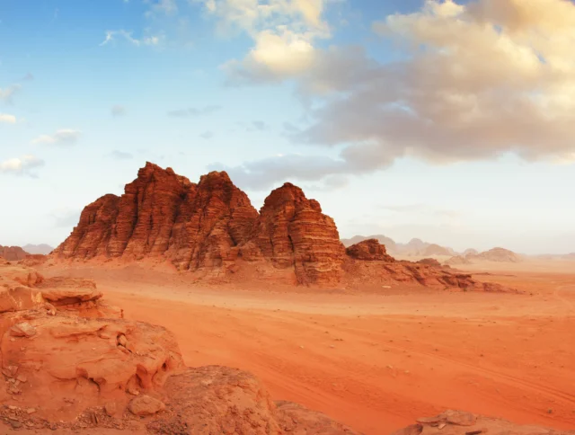 Rocky formations rise from a vast desert landscape under a partly cloudy sky.