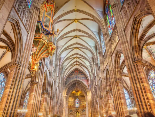 Interior of a cathedral with a vaulted ceiling, ornate organ, and colorful stained-glass windows.