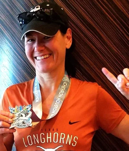 Person in an orange shirt holding a medal and making a hand gesture, smiling.