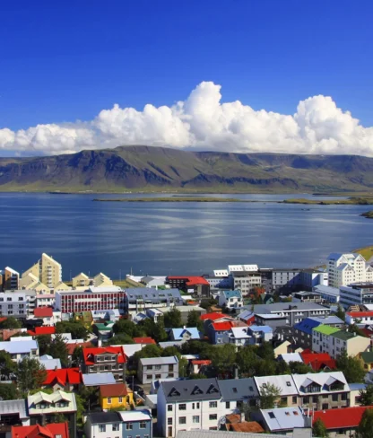 Colorful rooftops of a coastal town with a scenic view of a mountain range and a cloudy blue sky in the background.
