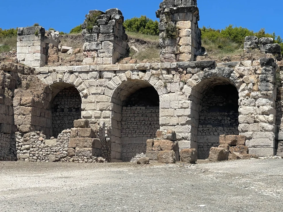 Ancient stone ruins with three large arched doorways and partial walls, set against a clear blue sky.