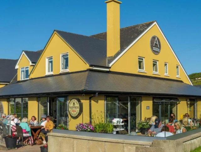 People sitting on a terrace outside a yellow building with a Guinness sign under a clear blue sky.