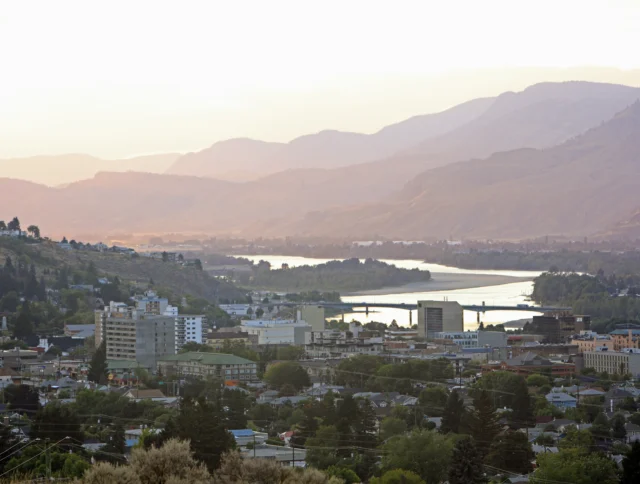 Aerial view of a city with a river running through it, surrounded by mountains during sunrise or sunset.