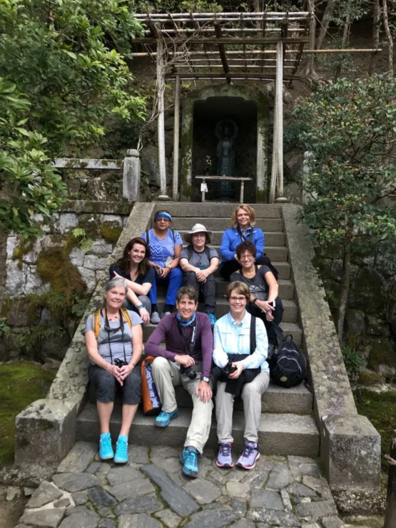 Group of eight people sitting on stone steps outside in a garden setting, with greenery and a small statue behind them.