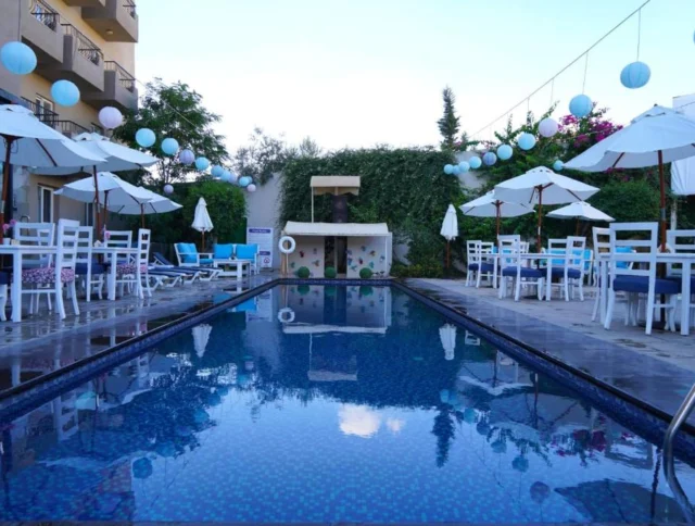 Outdoor pool surrounded by white chairs and umbrellas, with decorative lanterns hanging above.