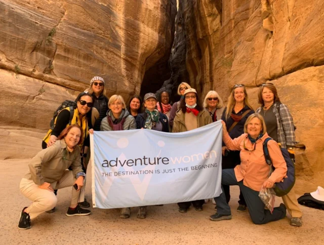 A group of women pose with an "Adventure Women" banner in a rocky canyon setting.