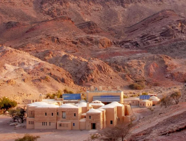 A cluster of beige buildings surrounded by rocky desert mountains under a clear sky.