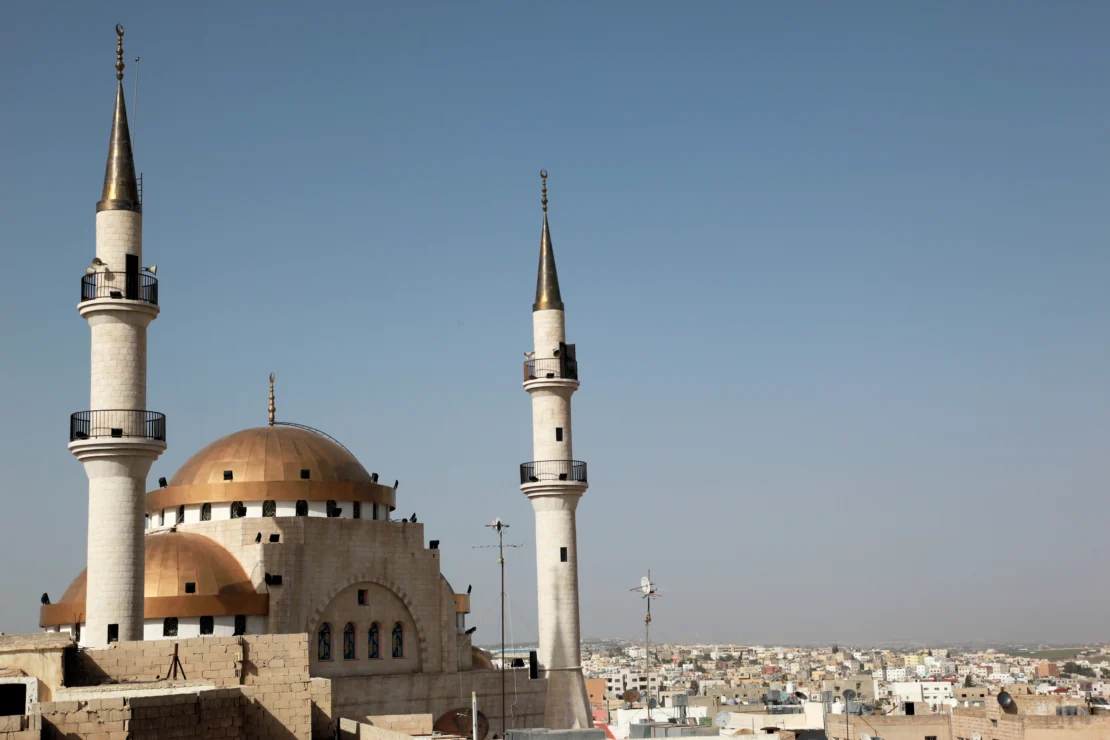 A mosque with two minarets against a clear blue sky, overlooking a cityscape.
