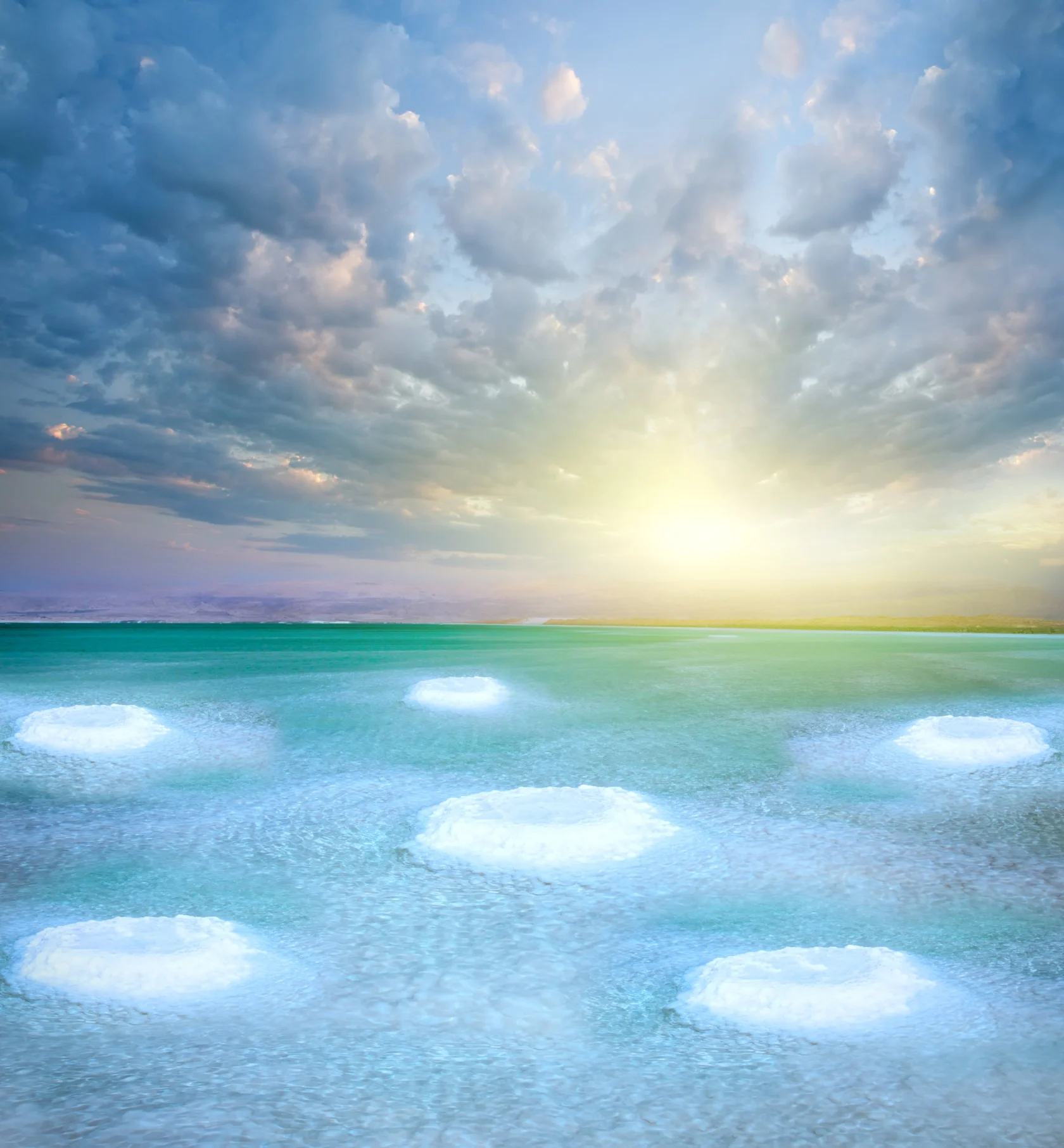 The image shows a serene ocean scene at sunrise, with several large white circular patterns in the water under a cloudy sky.