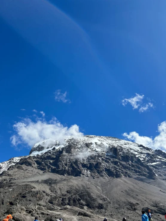 Snow-capped mountain peak under a clear blue sky with scattered clouds.