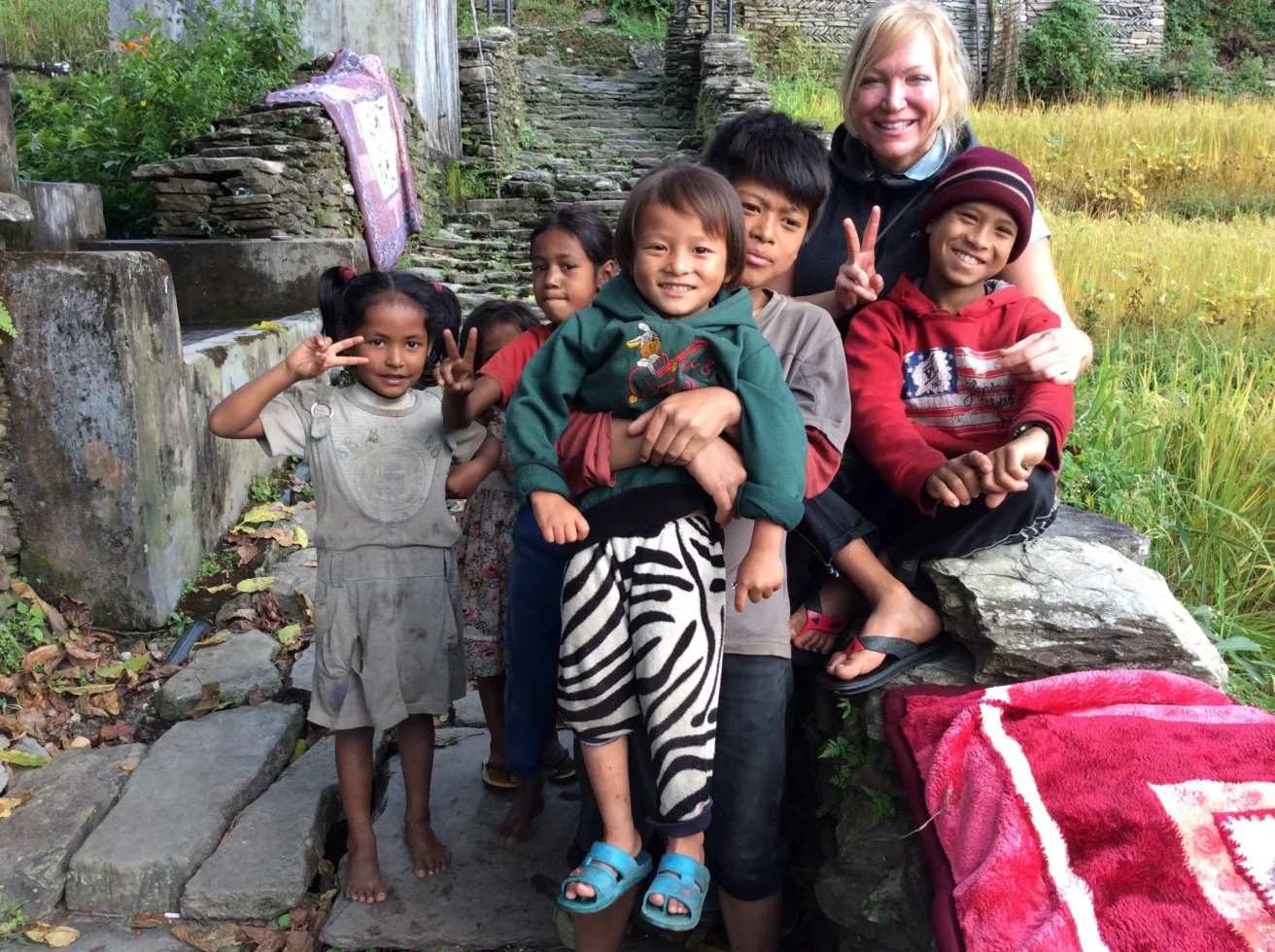 A group of children and an adult smiling, sitting on stone steps outdoors with greenery in the background.