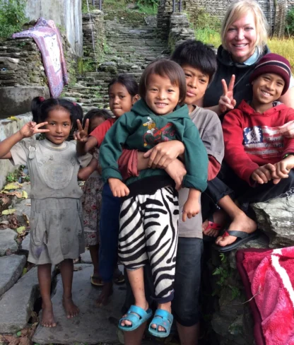 A group of children and an adult smiling, sitting on stone steps outdoors with greenery in the background.