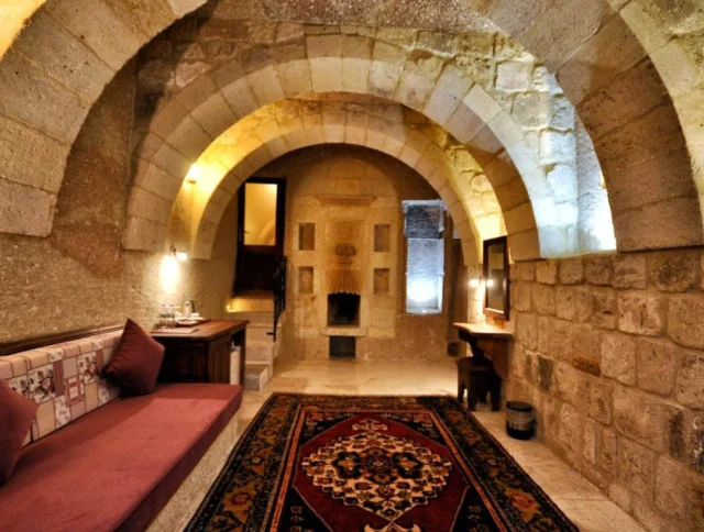 Stone interior with arched ceilings, a long cushioned bench, and a patterned rug on the floor. Walls and ceiling are made of textured stone blocks, illuminated by soft lighting.