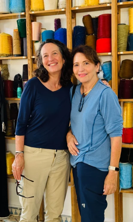 Two people smiling in front of shelves filled with colorful spools of thread.