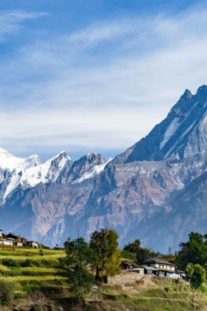 Scenic mountain landscape with snow-capped peaks and lush terraced fields, under a clear blue sky.