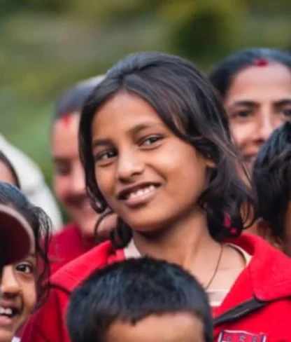 A group of smiling children and adults, some wearing red jackets, gather closely for a photo.