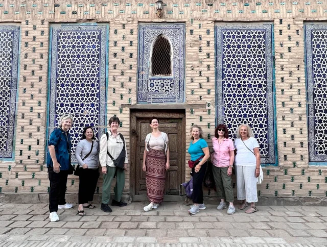 Seven people standing in front of a building with intricate blue and white tile work and a wooden door.