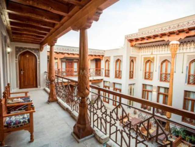 A hotel corridor with wooden railings and columns overlooks a central courtyard surrounded by two-story buildings featuring numerous windows with decorative wooden details.