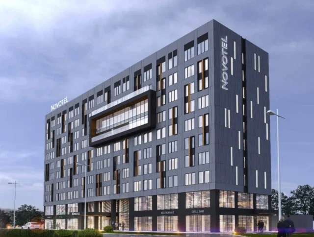 A modern Novotel hotel building with large windows and an overcast sky in the background.