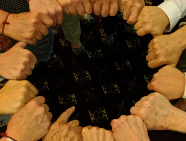 A group of people form a circle with their fists touching in the center.