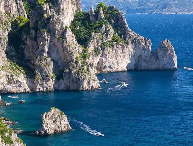 Rocky cliffs and several boats on the blue sea near a coastline.