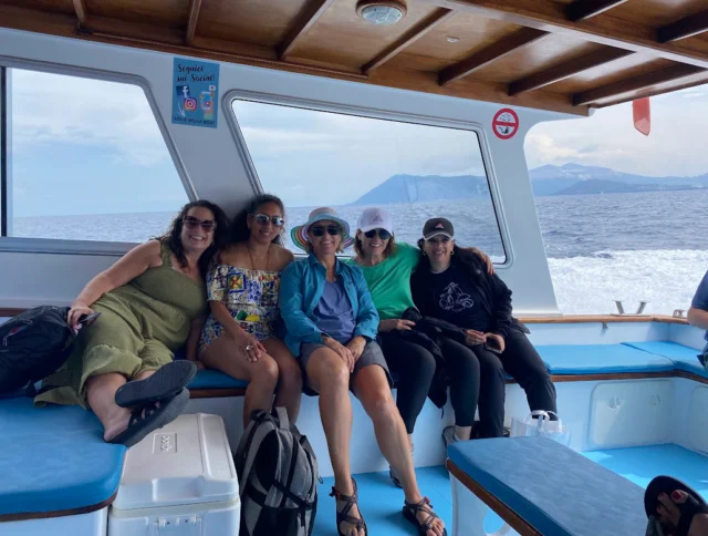 Five people sitting together on a boat bench with the ocean and mountains in the background.