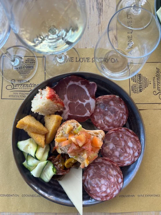 A plate with various meats, cheese, vegetable slices, and bread. Three empty wine glasses are partially visible above the plate.