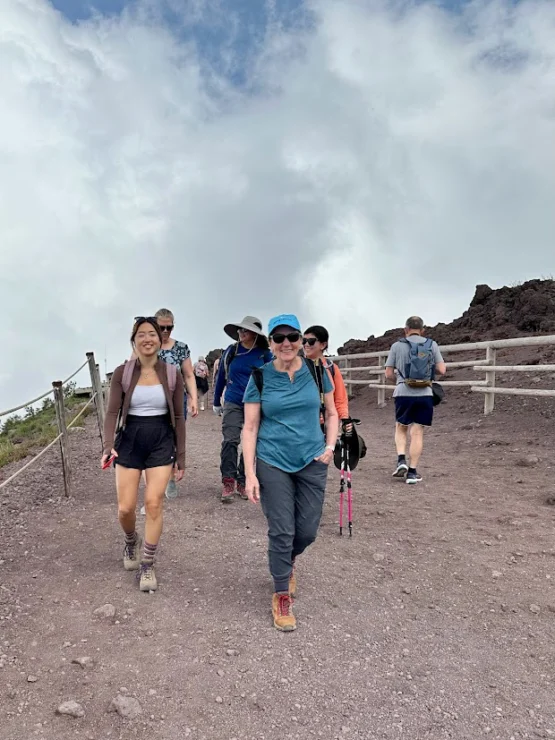 A group of hikers walking up a rocky trail on a cloudy day, some using trekking poles, with wooden rails on the side.