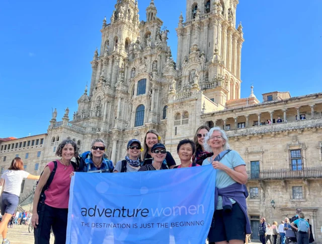 A group of women holding a banner reading "Adventure Women" in front of a historic cathedral with ornate spires under a clear blue sky.