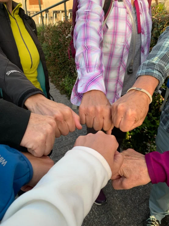 A group of seven people stand in a circle, each extending a fist towards the center, creating a gesture of unity or teamwork.