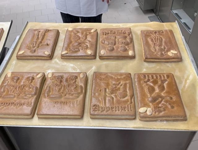 A tray with eight rectangular gingerbread cookies, each embossed with different designs and decorated with almonds, displayed on parchment paper.