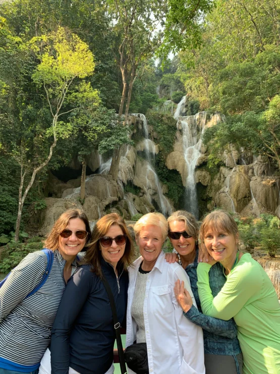 Five people smiling in front of a waterfall surrounded by lush greenery.
