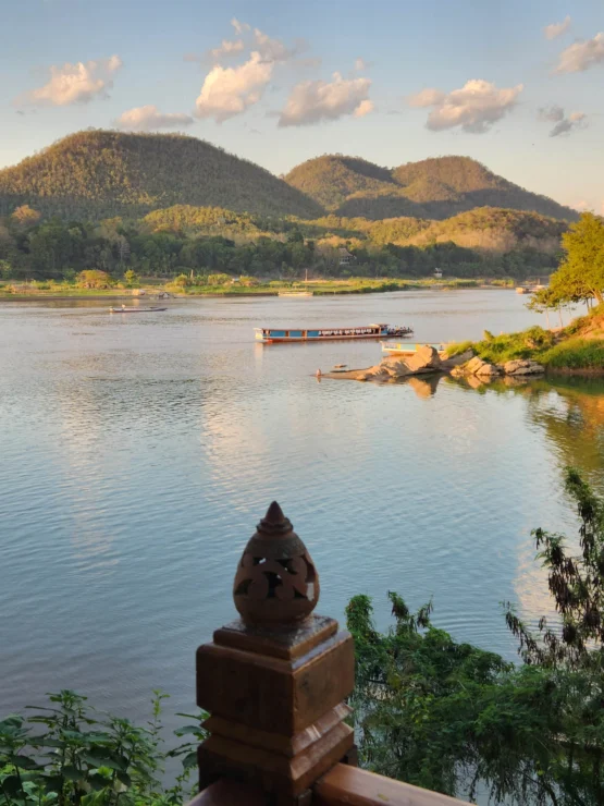 A scenic river view with hills in the background, a boat on the calm water, and a decorative wooden post in the foreground.