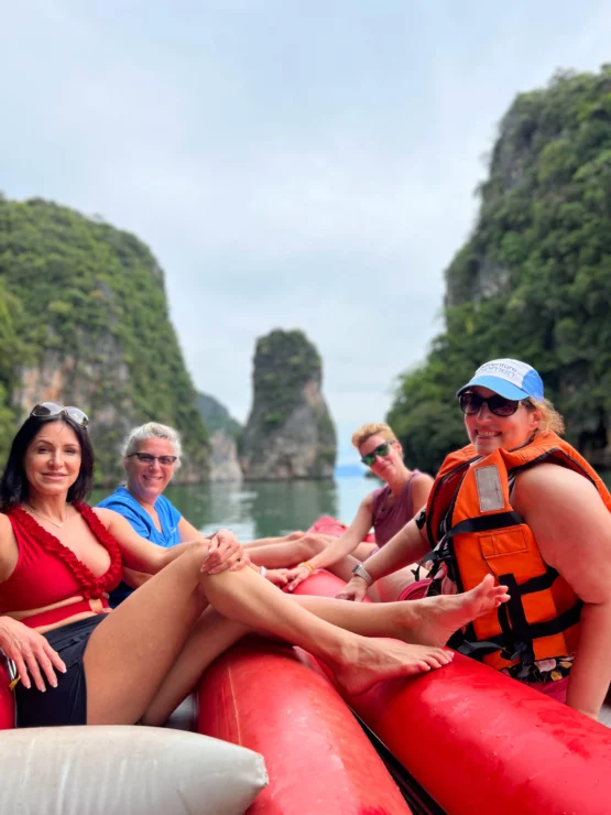 A group of people sit on a red inflatable raft surrounded by scenic limestone cliffs and greenery.